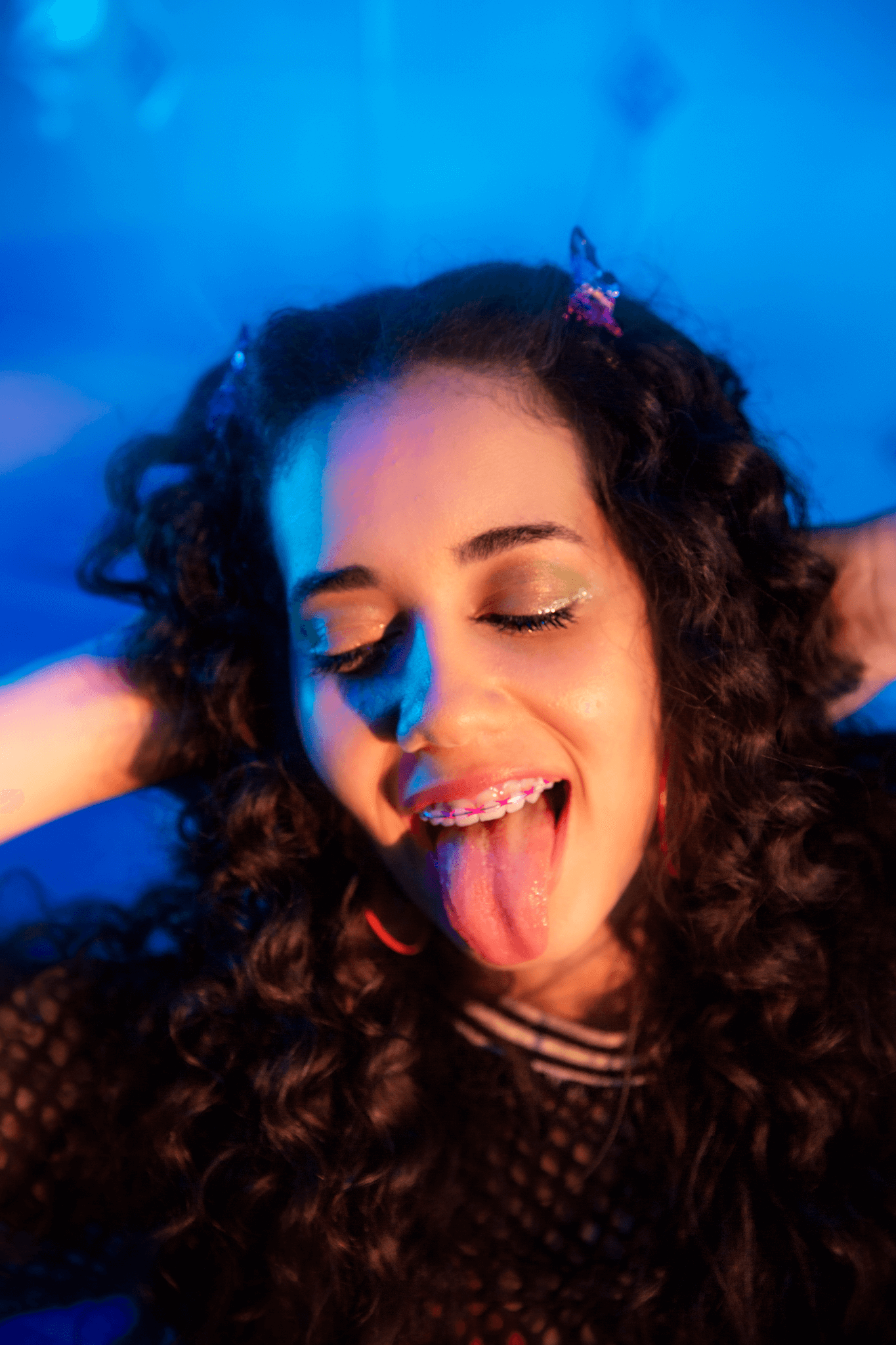 A young woman with long curly hair sticks out her tongue puts her hand behind her head to relax.